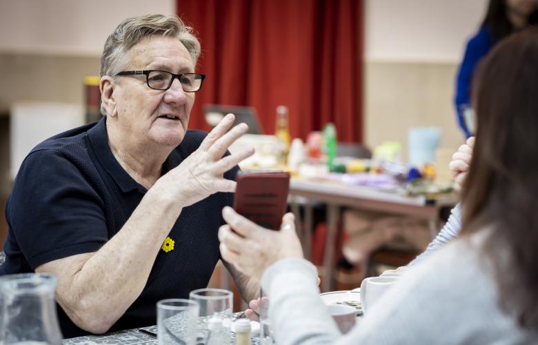 Man talking while someone shows him a phone.