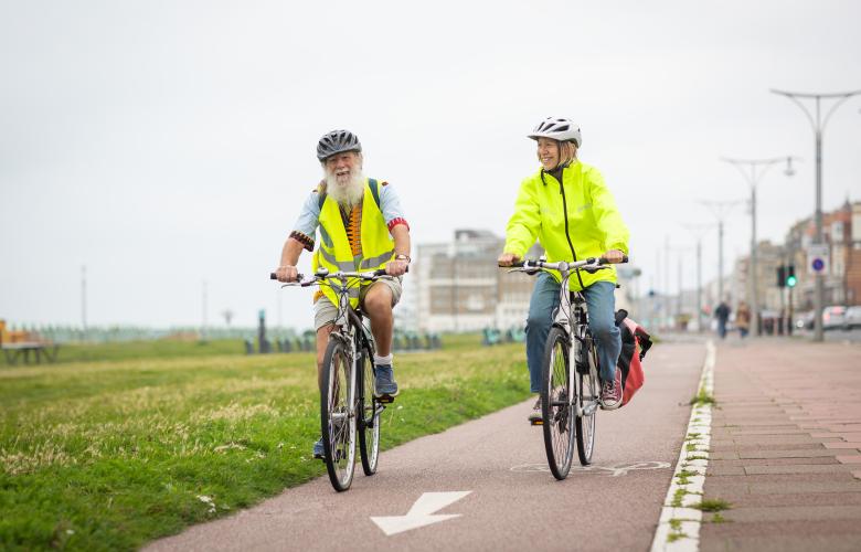 Two older adults cycling together along Brighton seafront.