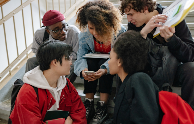 A group of young people sat together on a staircase looking at a phone.