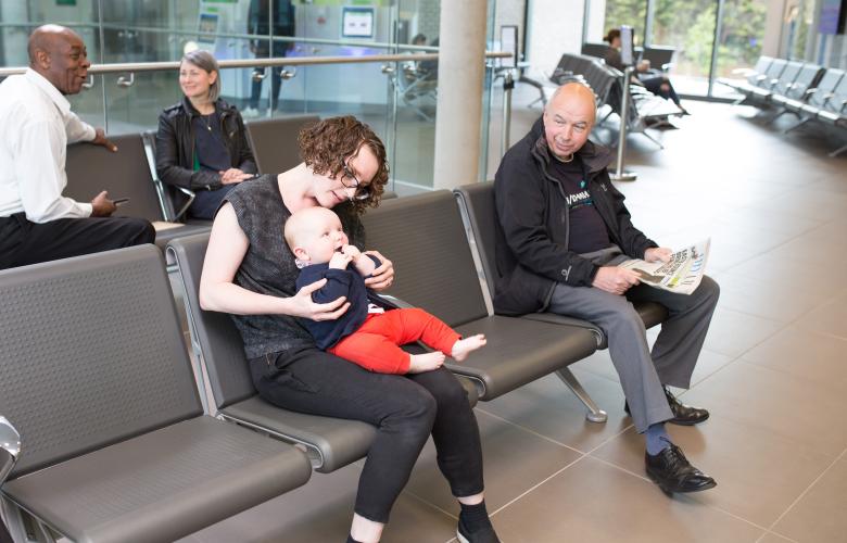 Several people in a clinical waiting room with one woman with a baby on her lap.