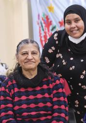 A young woman standing with an older woman sitting down.