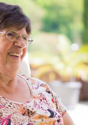 older woman sitting in chair by a garden smiling